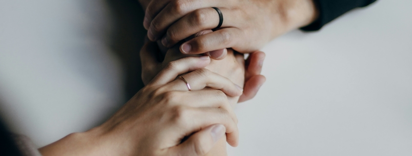 Two people are holding hands solemnly, conveying a sense of support and seriousness. This image relates to the cost to set up a living will, highlighting the importance of making informed decisions about medical treatment preferences and the associated expenses.