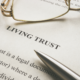 Close-up of a legal document labeled 'Living Trust' with a pen and glasses resting on the page, symbolizing estate planning and financial preparation.